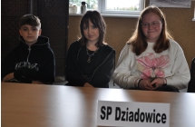 Dwie uśmiechnięte dziewczynki i chłopiec siedzący przy stole 