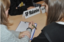 Uczniowie piszący na kartce. Siedzą przy stoliku 