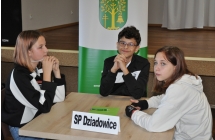 Uśmiechnięty chłopak wraz z dwiema dziewczynkami. Siedzą przy stoliku 