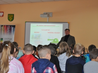 Mężczyzna stoi przed dużą grupą siedzących dzieci