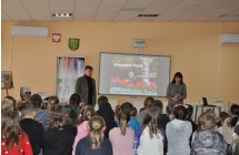 Mężczyzna i kobieta stoją przed grupą siedzących dzieci. W tle kolorowy slajd