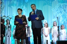 Konferansjerzy - kobieta i mężczyzna stojący na scenie. Za nimi dzieci przebrane za aniołki 