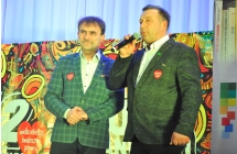 Dwoje mężczyzn na scenie, jeden mówi do mikrofonu 