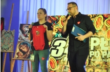 Mężczyzna i kobieta na scenie - prowadzący licytacje. Kobieta trzyma dziecięce body 