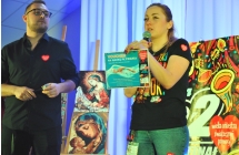 Kobieta i mężczyzna na scenie. Kobieta trzyma w ręce voucher i mówi do mikrofonu 