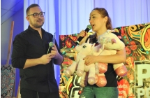 Kobieta i mężczyzna na scenie. Kobieta trzyma licytowany przedmiot - dwa pluszowe jednorożce 