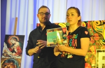 Kobieta i mężczyzna na scenie. Kobieta trzyma licytowany przedmiot - voucher 