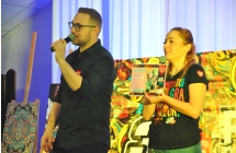 Kobieta i mężczyzna na scenie - kobieta prezentuje licytowany przedmiot - voucher 