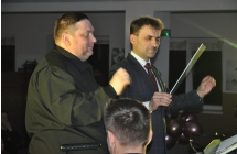 Dwoje mężczyzn na scenie. Jeden z nich dyryguje batutą zespół 