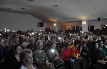 Kilkaset osób siedzących na krzesełkach na sali CKiBP w Malanowie. Większość w podniesionych rękach trzyma telefony z zapalonymi latarkami