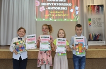 Dwie dziewczynki i dwoje chłopców z dyplomami przed sceną 