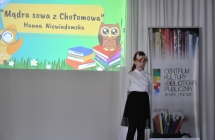 Dziewczynka recytująca wiersz na scenie. Za nią  wyświetlona grafika i baner z napisem - Centrum Kultury i Biblioteka Publiczna w Malanowie 