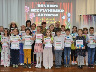 Kilkanaście dzieci oraz kobieta. Dzieci biorący udział w konkursie recytatorskim 