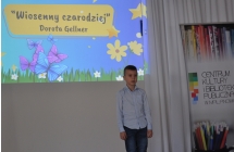 Chłopiec recytujący wiersz na scenie. Za nim wyświetlana grafika 