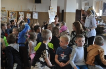 Dzieci siedza na krzesłach, kobieta w stroju zająca pokazuje im maskę wilka