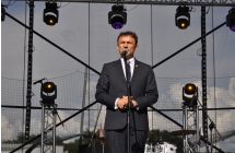 Mężczyzna w garniturze przemawia na scenie do mikrofonu 