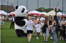 Wielkogabarytowy miś panda na placu imprezy. Wokół niego wiele dzieci i dorosłych 