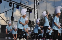 Kilkanaście dziewczynek tańczących na scenie. Ubrane mają kapelusze a'la smerfy 