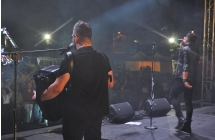 Instrumentaliści oraz wokalista na scenie. Przed nimi tłum fanów 