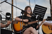 Dziewczyna grająca na gitarze. Obok niej dwoje innych gitarzystów 