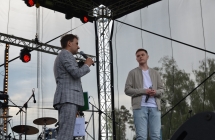 Dwoje mężczyzn na scenie. Jeden z nich mówi do mikrofonu 