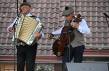 Dwoje muzyków w ludowych strojach. Jeden gra na akordeonie, drugi na basach kaliskich 