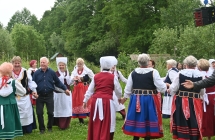 Kilkunastu śpiewaków w ludowych strojach tańczących na parkiecie pod sceną 