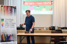 Pisarz podczas spotkania autorskiego. Za nim na scenie wyświetla się slajd 