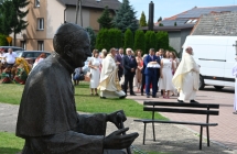 Korowód dożynkowy pod budynkiem kościoła. Na pierwszym planie pomnik papieża 