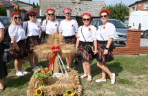 Uśmiechnięte kobiety w ludowych strojach prezentujące wieniec dożynkowy 