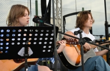 Dwie dziewczyny na scenie. Obydwie grają na gitarach, jedna dodatkowo śpiewa do mikrofonu 