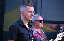 Mężczyzna grający na gitarze basowej, w tle kobieta śpiewająca chórki 