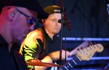 Dwoje mężczyzn. Jeden grający na gitarz elektrycznej, drugi na perkusji. 