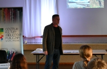 Mężczyzna stojący przy scenie. Obok niego baner z napisem - Centrum Kultury i Biblioteka Publiczna w Malanowie 