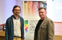 Dwoje uśmiechniętych mężczyzn na tle sceny i baneru - centrum kultury i biblioteka publiczna w malanowie 