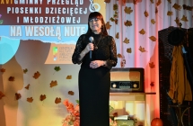 Kobieta w eleganckim stroju na scenie mówiąca do mikrofonu 