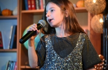 Dziewczynka w sukience z cekinami śpiewająca do mikrofonu ze sceny 