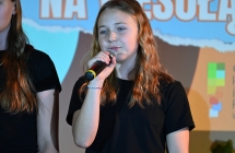 Dziewczynka skupiona na wokalnym wykonaniu utworu. Trzyma mikrofon i śpiewa.