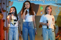 Trzy dziewczynki śpiewające do mikrofonów ze sceny 