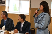 Kobieta mówiąca do mikrofonu. Obok siedzi dwójka mężczyzn 