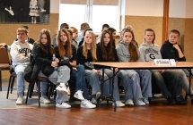Grupa uczniów siedzących na krzesełkach przy stole 