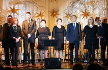 Kilkanaście elegancko ubranych osób śpiewających na scenie 