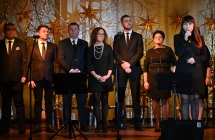 Kobieta mówiąca do mikrofonu. Za nią stoi kilkanaście osób 
