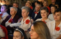 Kilkadziesiąt osób siedzących na krzesłach. Na pierwszym planie kobiety z zespołu ludowego 