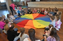 Kilkudziesięcioro dzieci siedzących przy chuście edukacyjnej 