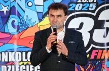 Elegancko ubrany mężczyzna mówiący do mikrofonu na scenie. Za nim plakat z napisem - 33. Finał Wielkiej Orkiestry Świątecznej Pomocy 