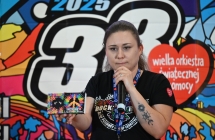 Kobieta mówiąca do mikrofonu. W drugiej ręce trzyma kalendarz przeznaczony na licytację 