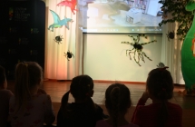 Dzieci na tle scenografii scenicznej - pająk i wyświetlane dinozaury 