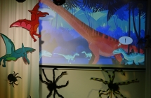 Dinozaur wyświetlony na ekranie i dwa latające dinozaury przywieszone do kotary 