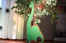 Makieta dinozaura stojąca przy drzewku 